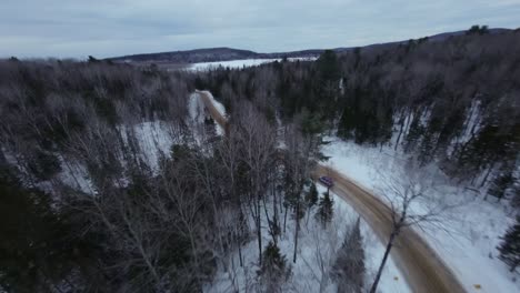 aerial view of a car driving on a snowy road through a winter forest