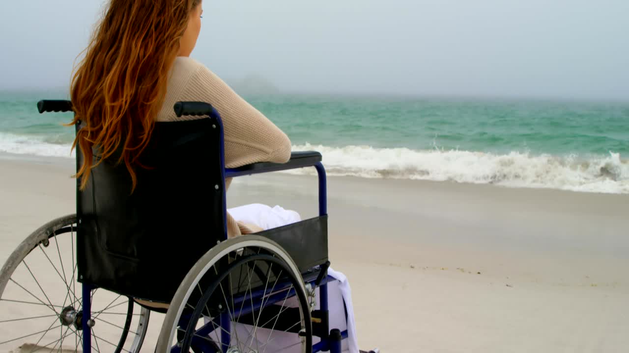 Rear view of woman sitting on wheelchair at beach 4k