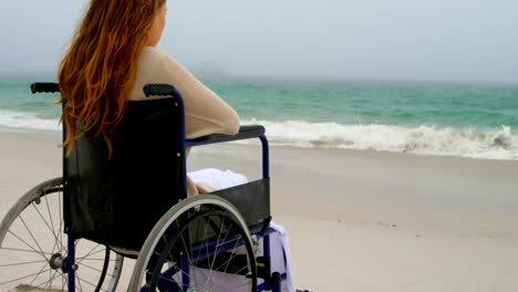 vista trasera de una mujer sentada en silla de ruedas en la playa 4k
