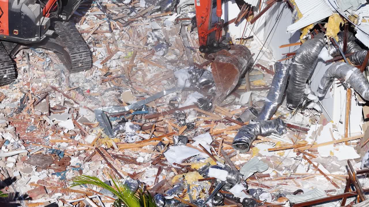 An excavator uses its bucket to demolish a house, scattering debris and dust in a sunlit construction site on the Gold Coast, Australia