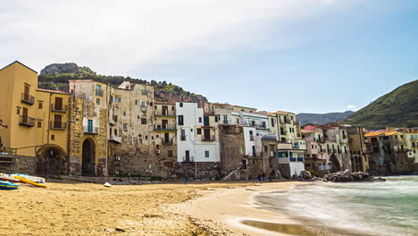 Una-Cadena-De-Edificios-Antiguos-En-Una-Costa-Con-Montañas-Al-Fondo-En-Sicilia.