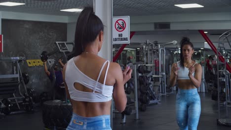 female bodybuilder flexing her muscles with her mirror reflection at the gym