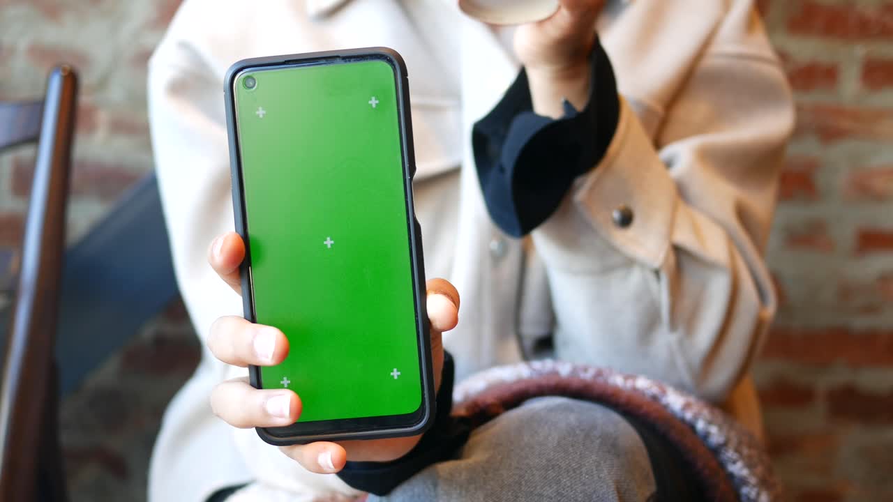 mujer sosteniendo un teléfono inteligente con pantalla verde en un café