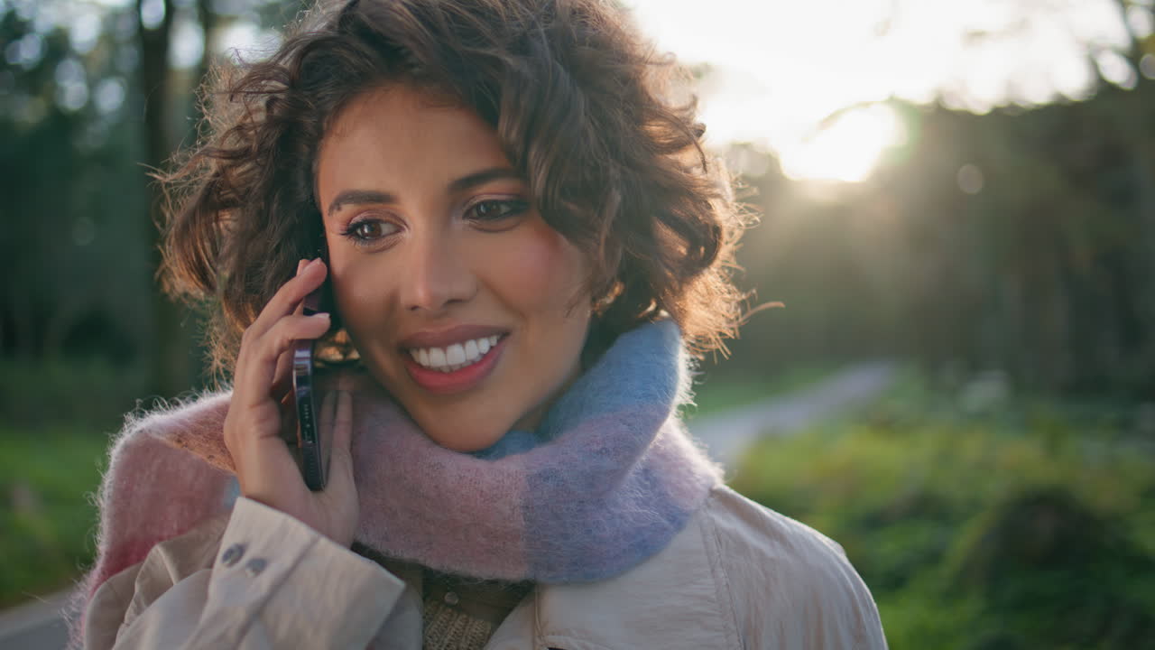 Smiling woman talking smartphone in sunlight-drenched forest closeup portrait