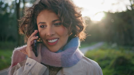 smiling woman talking smartphone in sunlight-drenched forest closeup portrait