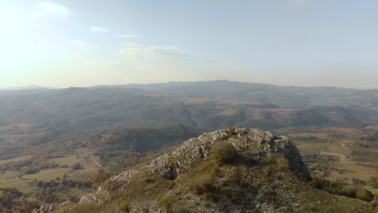 rastreando una toma aérea sobre una colina rocosa, un valle verde como fondo