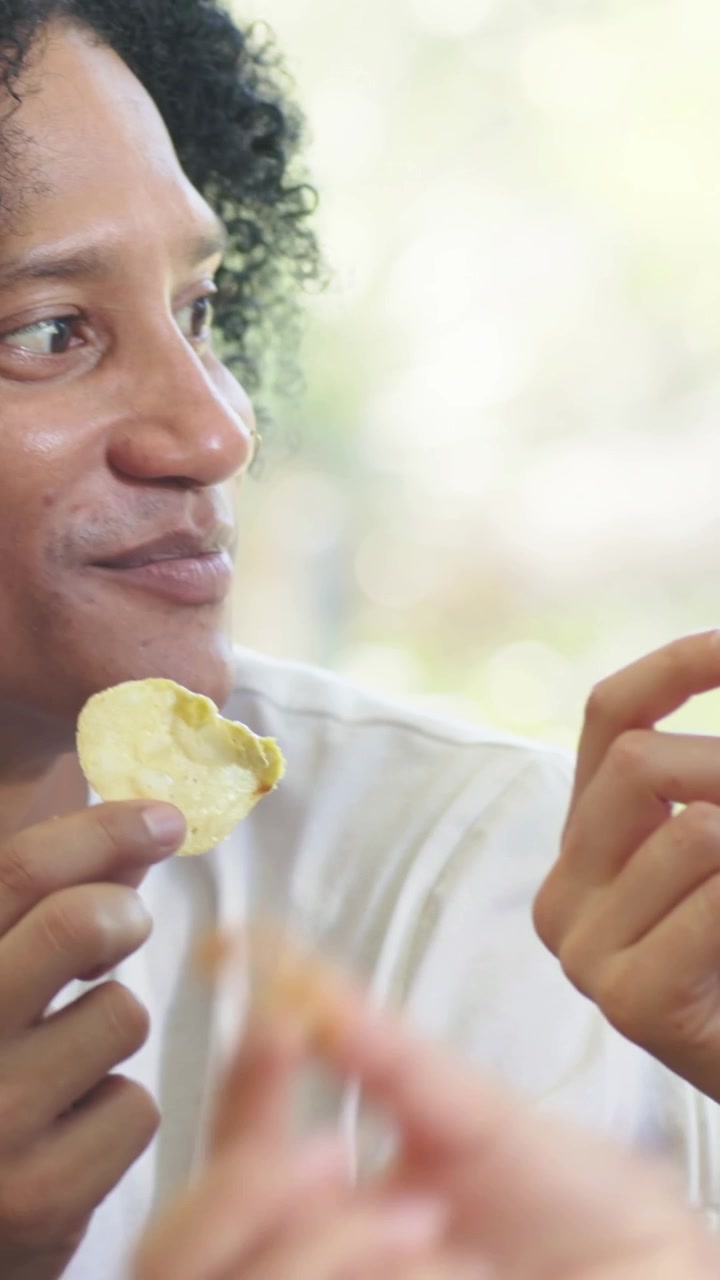 Vídeo vertical: Mulher de blusa vermelha reagindo e conversando, compartilhando lanche à mesa, mão com salgadinho, com espaço para texto.
