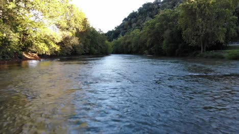 drone vuela bajo sobre un río con un reflejo de los árboles a ambos lados del río