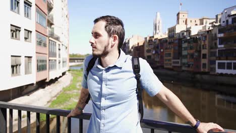 Tourist-in-Girona-looking-around-the-bridge,-colorful-houses-at-the-background,-clear-sky,-Spain,-slow-motion