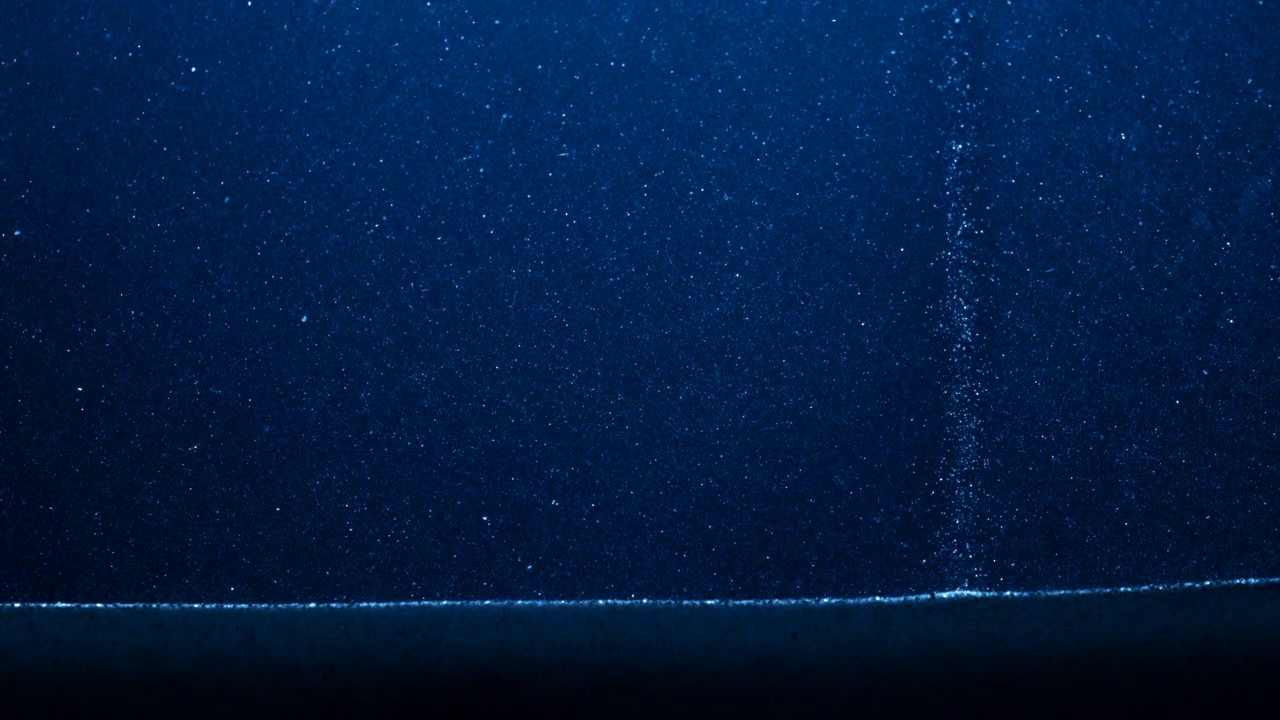 Dusty particles falling under blue night light in abstract slow motion