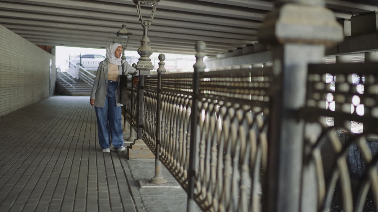 черная мусульманка отдыхает возле поручня на городской набережной