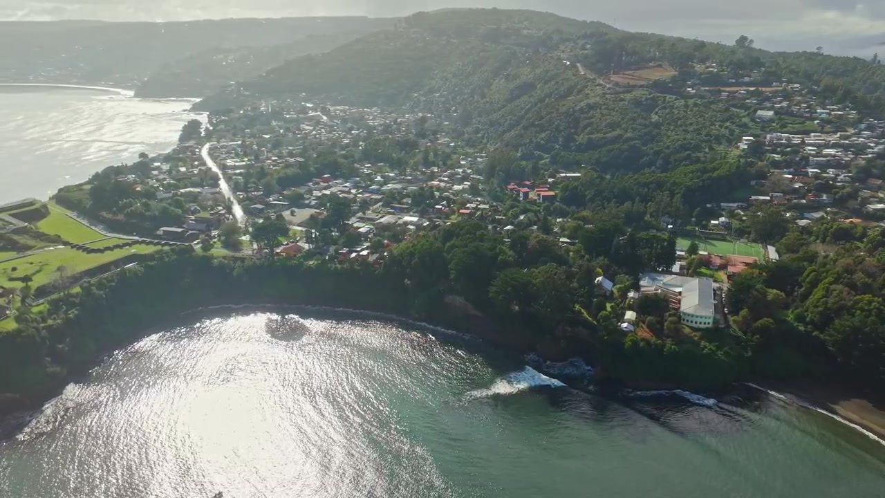 Dolly aéreo hacia atrás del pueblo costero de Niebla y colinas boscosas en Valdivia, Chile