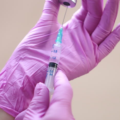 Close-up view on a cosmetologists hands in gloves holding syringe with needle for rejuvenating facial injections.
