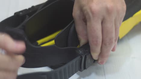 close-up of a woman’s hands adjusting the heel straps on scuba diving fins, ensuring a secure and comfortable fit before entering the water