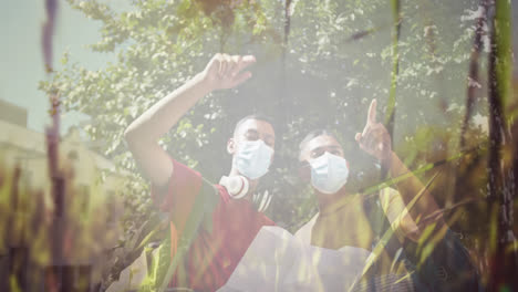 composite of happy mixed race male friends in face masks reading map, and sunlight on trees