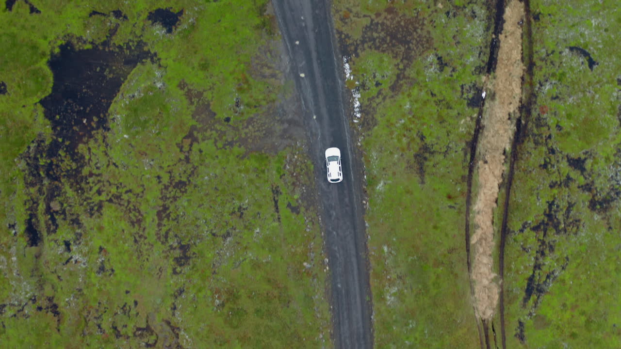 antena de arriba hacia abajo de un coche blanco en un camino de tierra fangoso con baches