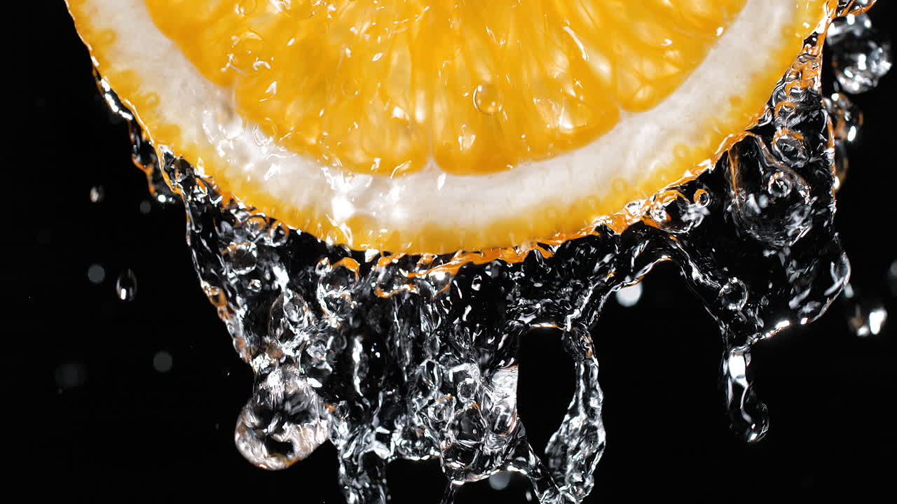 Fetta d'arancia irrorata d'acqua al rallentatore e in macro su sfondo nero