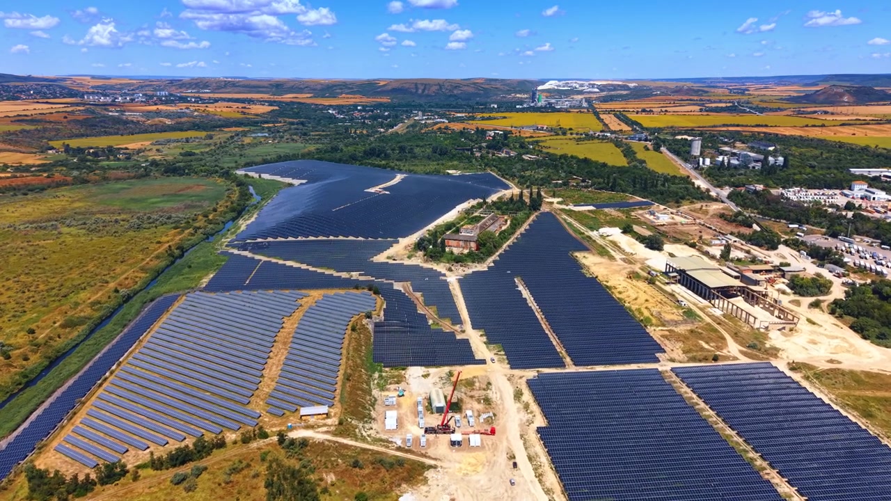 Vista aerea di centrale solare fotovoltaica in paesaggio rurale. Moduli fotovoltaici blu installati vicino a campi verdi e un fiume sotto un cielo sereno e soleggiato, ripresa con drone dall'alto