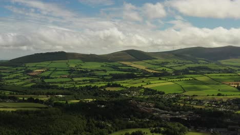 Irish-rural-landscape,-Aughrim,-Wicklow-August-2020,-Drone-gradually-tracks-parallel-to-village-facing-South-towards-Ballycoog-Upper-hills