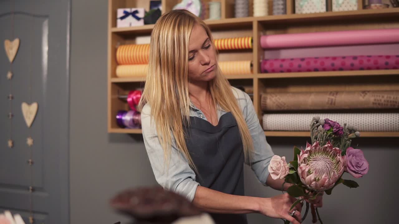Professional blonde female floral artist arranging beautiful bouquet at flower shot. She is combining different flowers together
