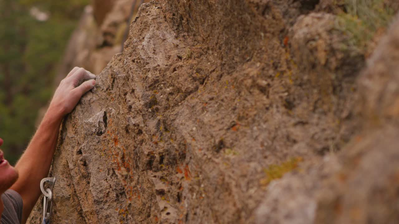 un escalador sopla tiza de sus dedos mientras escala una pared