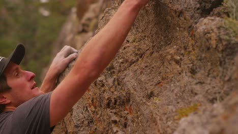 a rock climber blows chalk from his fingers as he scales a wall