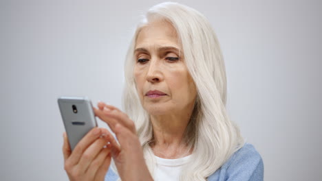 senior woman looking mobile phone indoors. old lady reading smartphone in studio