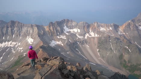 mountaineer with helmet walking on top of mountain summit with magnificent view of valley and range