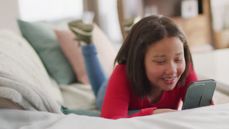 Video-of-happy-asian-girl-resting-on-sofa-with-smartphone