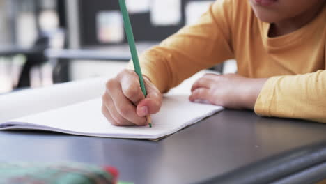 En-Un-Entorno-Escolar,-Un-Joven-Estudiante-Birracial-Se-Centra-En-La-Escritura.