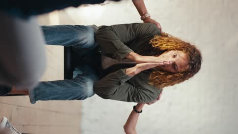 Vertical-video:-Sad-and-thoughtful-man-with-curly-hair-in-a-green-jacket-talks-about-his-problem-during-group-therapy.-The-rest-of-the-group-therapy-participants-support-the-man-and-stroke-his-shoulder