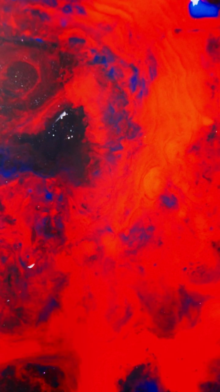 Swirling dark ink patterns spread in vivid red liquid, creating cosmic abstract shapes