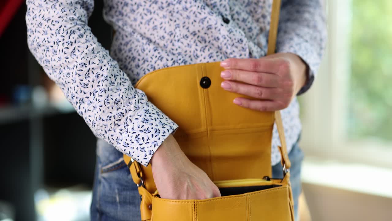 Person interacting with a yellow crossbody bag, putting in or taking out items