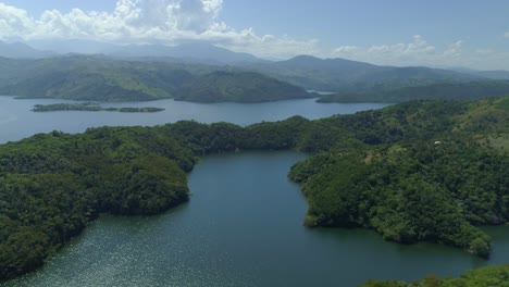 gorgeous blue water lakes surrounded by hills with lush green trees and foliage with cordillera central mountain range in background, overhead rising aerial