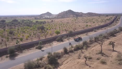 Landwirtschaftlicher-LKW,-Der-Auf-Der-Langen-Asphaltstraße-Durch-Das-Karge-Land-In-Rajasthan,-Indien-Fährt---Luftaufnahme