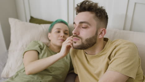 loving woman touching her boyfriend's face while relaxing on the bed at home