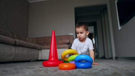 baby boy sitting on the floor on his knees building a pyramid. toddler child playing at home alone.