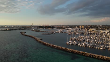 aerial approaching shot of fishing boat harbour in fremantle city during golden hour - western australia and industrial port in background