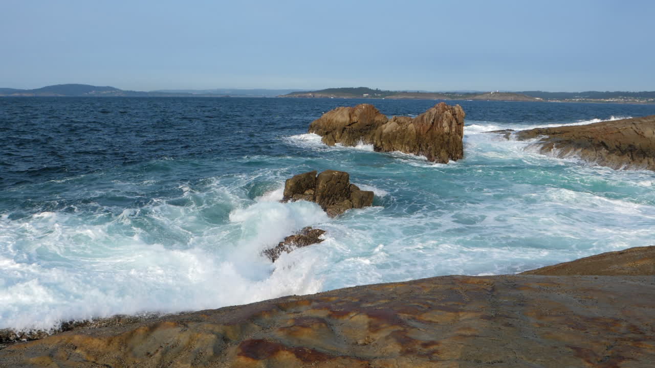paisaje marino con olas ásperas rompiendo en la orilla rocosa, día soleado slomo