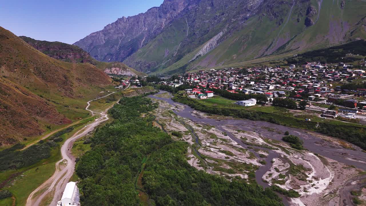 Aerial of Georgian remote settlement in valley with glacial stream meandering and creation flowing patterns