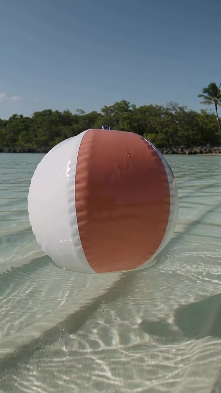 Vertical video: Floating inflatable beach ball bobbing over shallow coastal inlet, pushed by breeze