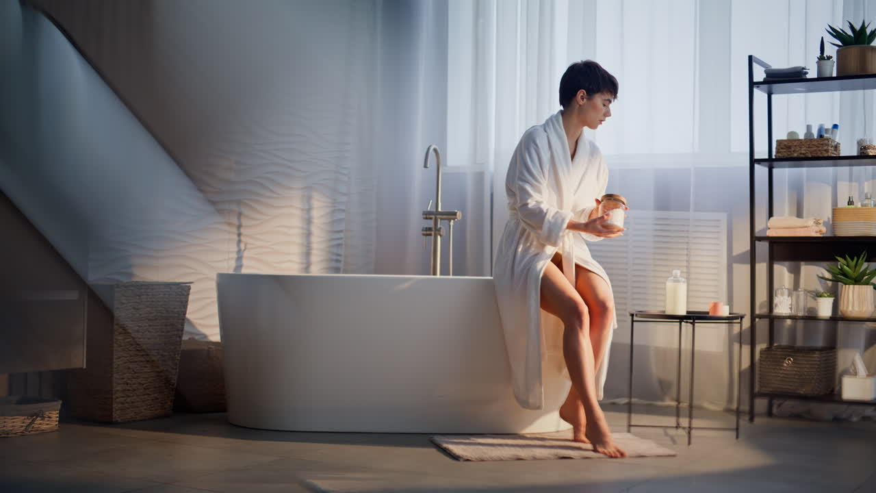 Tranquil brunette sitting tub dipping fingers checking water warmth in soft room