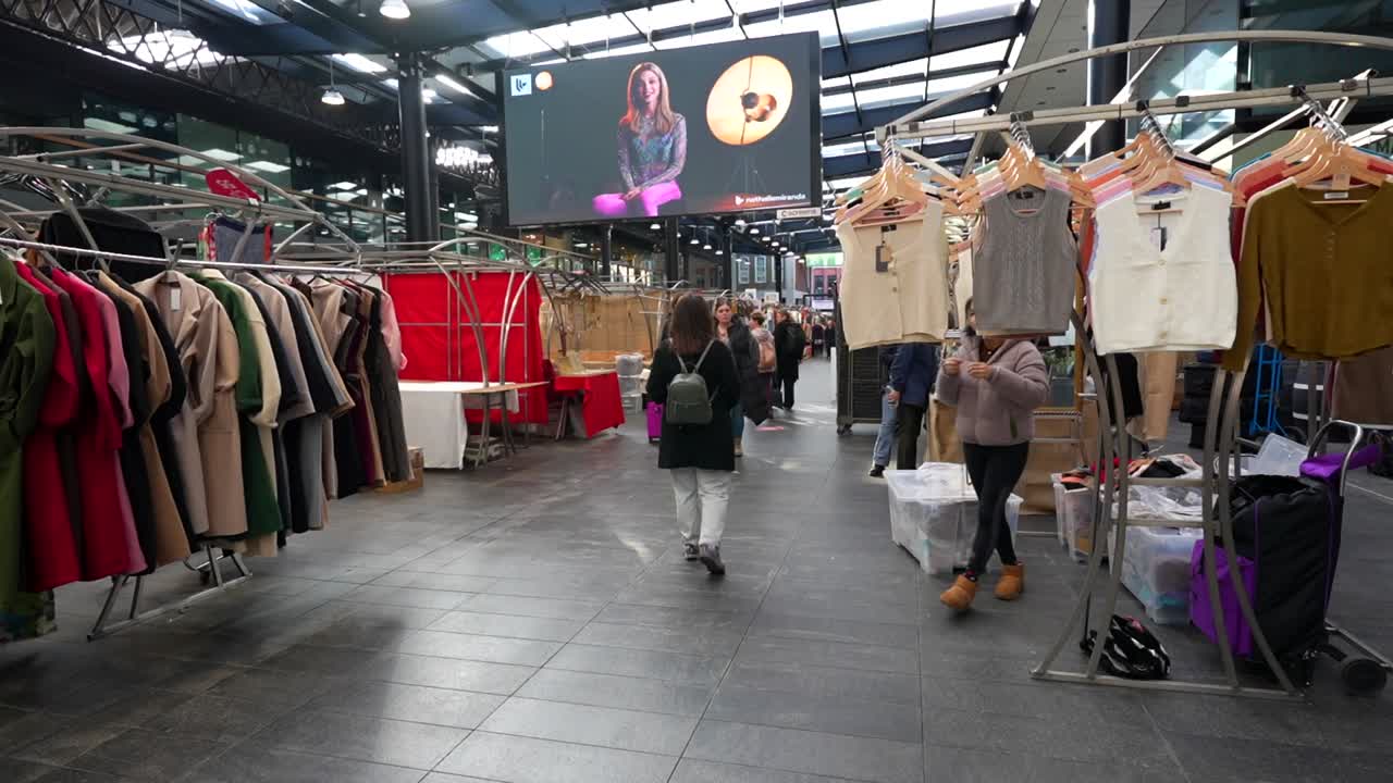 Tourist explores London's Spitalfields Market as a vendor arranges clothing on display