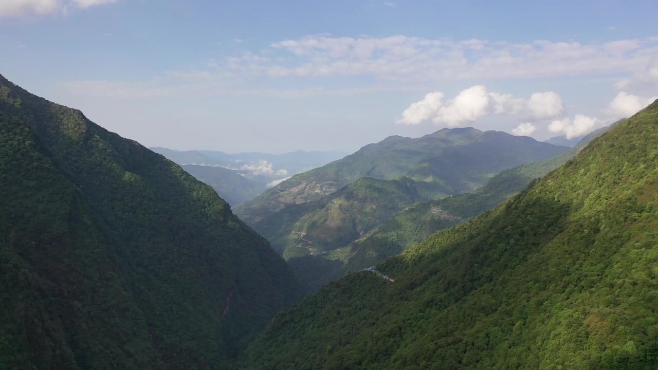 ネパールの広大な緑の山岳地帯の谷と森林に覆われた丘陵地帯を捉えた、息をのむような広角ドローンショット。晴れた夏の空の下、尾根の高くに小さな人里離れた村が佇んでいます