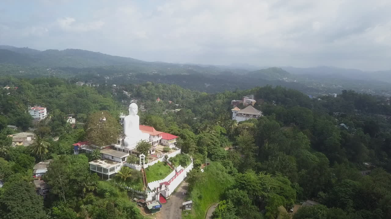 Aerial: Bright white Buddha statue overlooks Kandy city in Sri Lanka