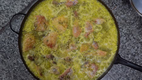 vista superior de una deliciosa paella española con guisantes, pollo y arroz hirviendo a fuego lento en una sartén grande en la cocina, de cerca