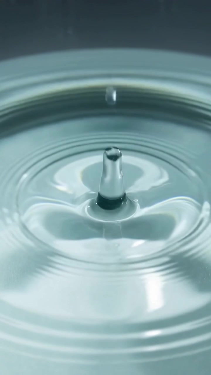 Video verticale: Flusso di liquido che cade sollevando una colonna centrale e una gocciolina in una ciotola da studio, increspandosi.
