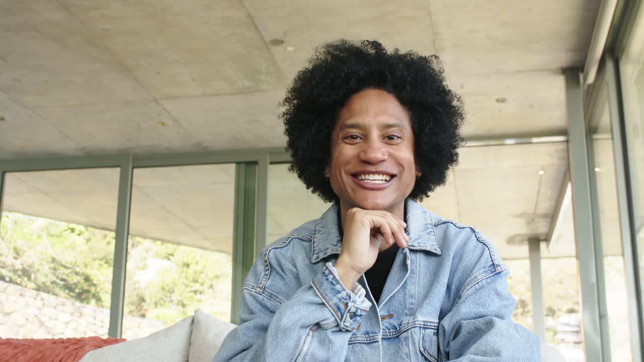 African American man resting chin on hand softly smiling then leaning forward and laughing on sofa