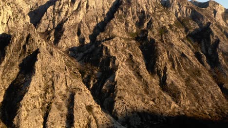 AERIAL---Sunbathed-mountains-around-Kotor,-Montenegro,-rising-shot