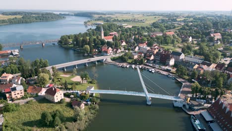 mikolajki, polonia: una vista aérea de aves en vuelo redondo desde el puente peatonal con mayor sabiduría y rotación sobre el panorama de la ciudad turística en warmian masuria con lago azul